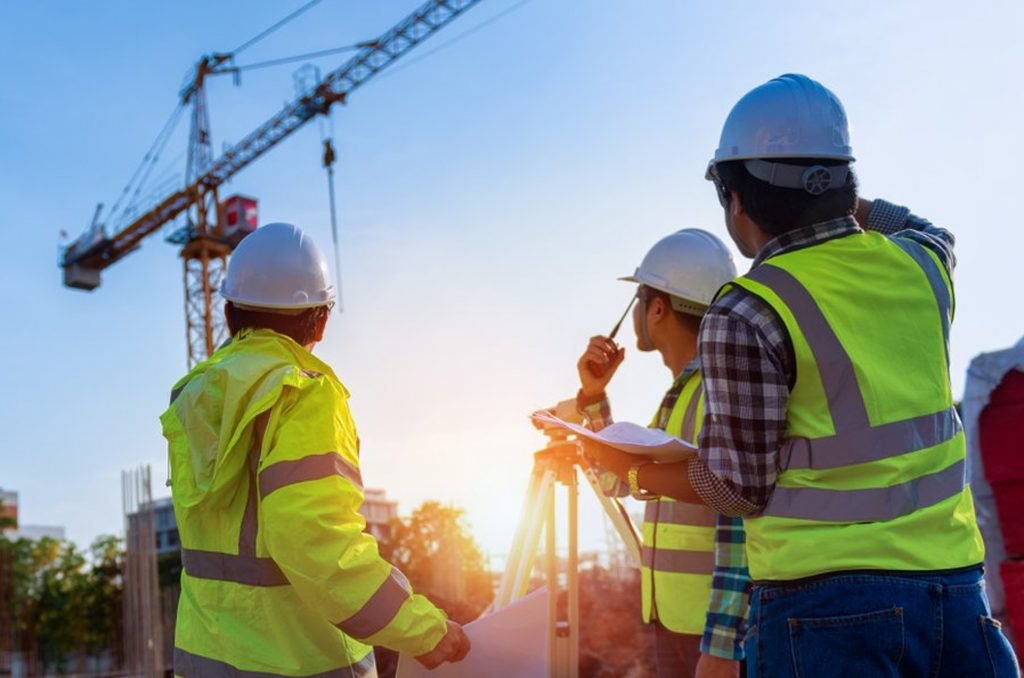 Tres ingenieros con chaleco supervisan una obra con grúa